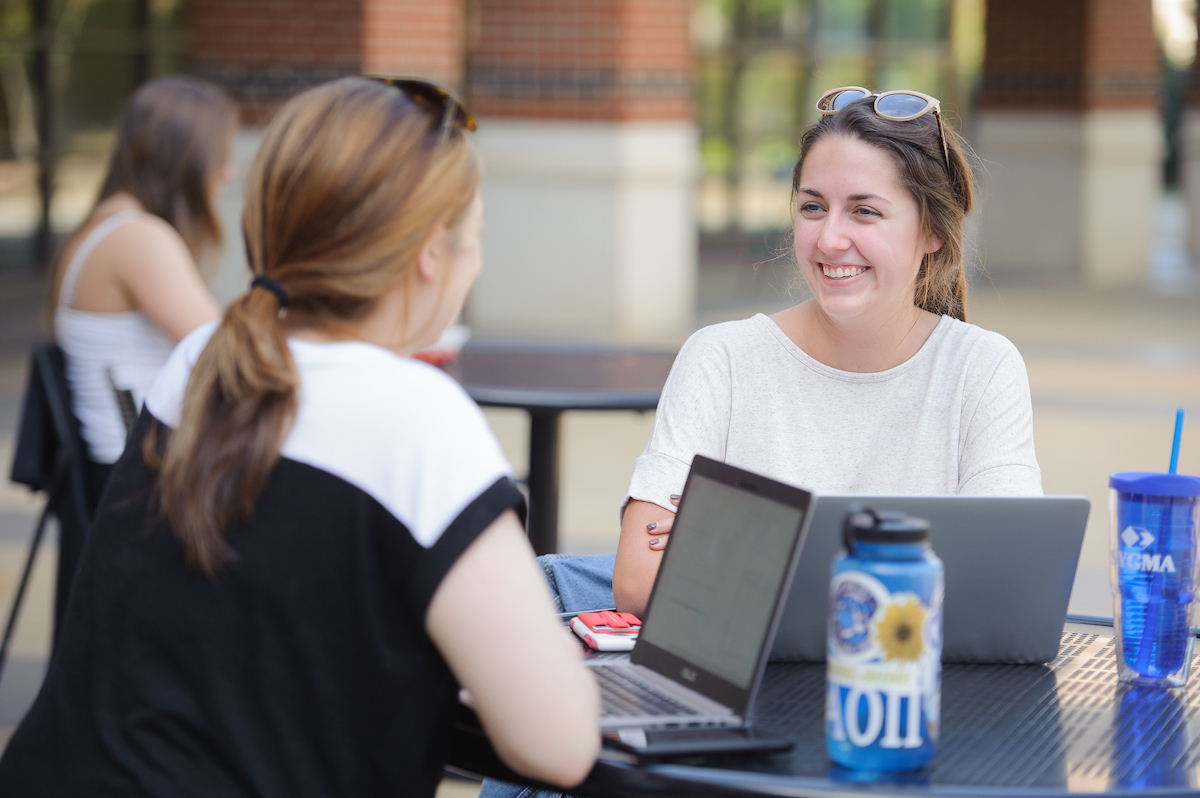 Two women sitting at a table outside of the Student Center.